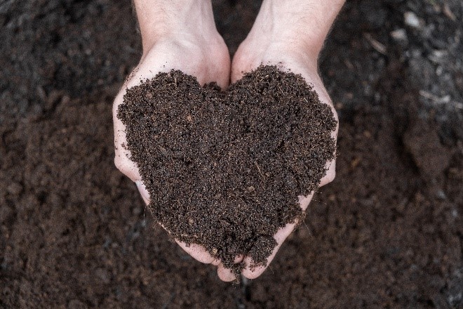 Twee handen samen met compst erop vormen een hartje met  op de achtergond compost